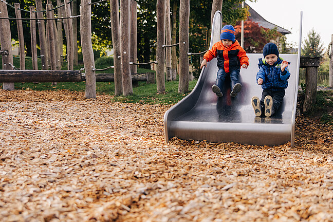 Kinder rutschen die Rutschbahn runter unten sind Fallschutzschnitzel